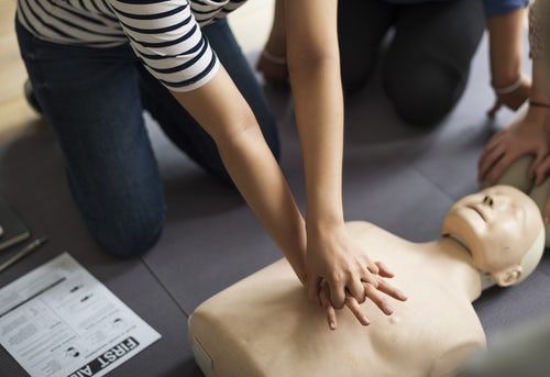 Eine Person ist über eine Puppe gebeugt und simuliert erste Hilfe durch Herzdruck Massage.