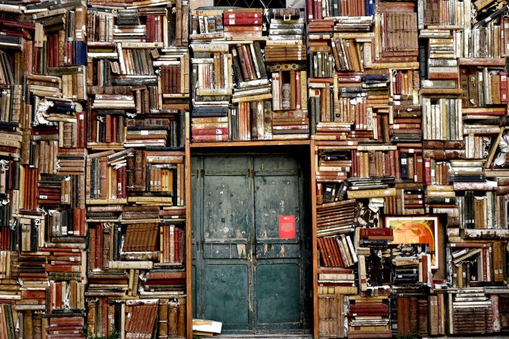 Wand voller Bücher, die quer gestapelt sind. In der Mitte befindet sich eine Tür