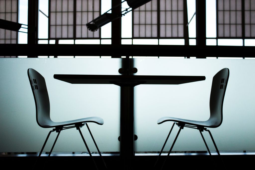 Seitenansicht: 2 Stühle und ein Tisch vor einer halbhohen Milchglaswand und einem Fenster