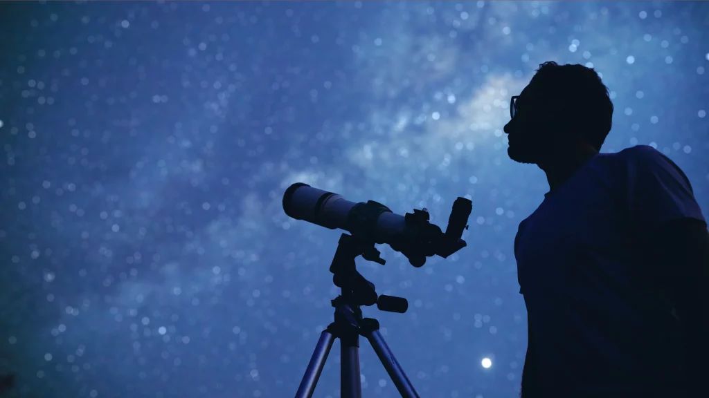 Mann schaut durch ein Teleskop in den Himmel. Blick festhalten. Dokumentieren.